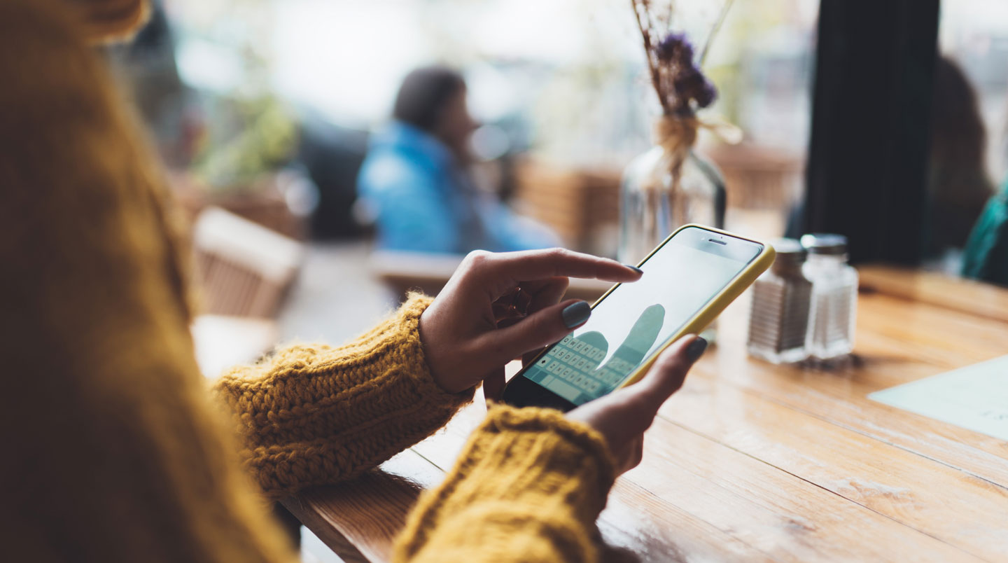 Une femme dans un café moderne consulte sur son smartphone un formulaire de demande de crédit en ligne, dans une ambiance lumineuse et détendue